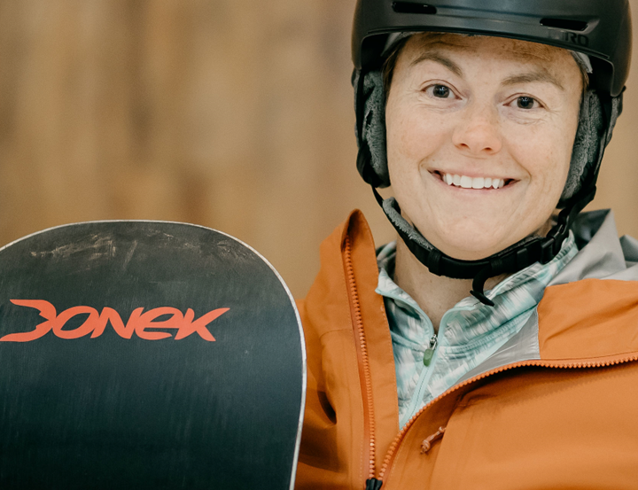 Person wearing a helmet and holding a snowboard with a blurred background